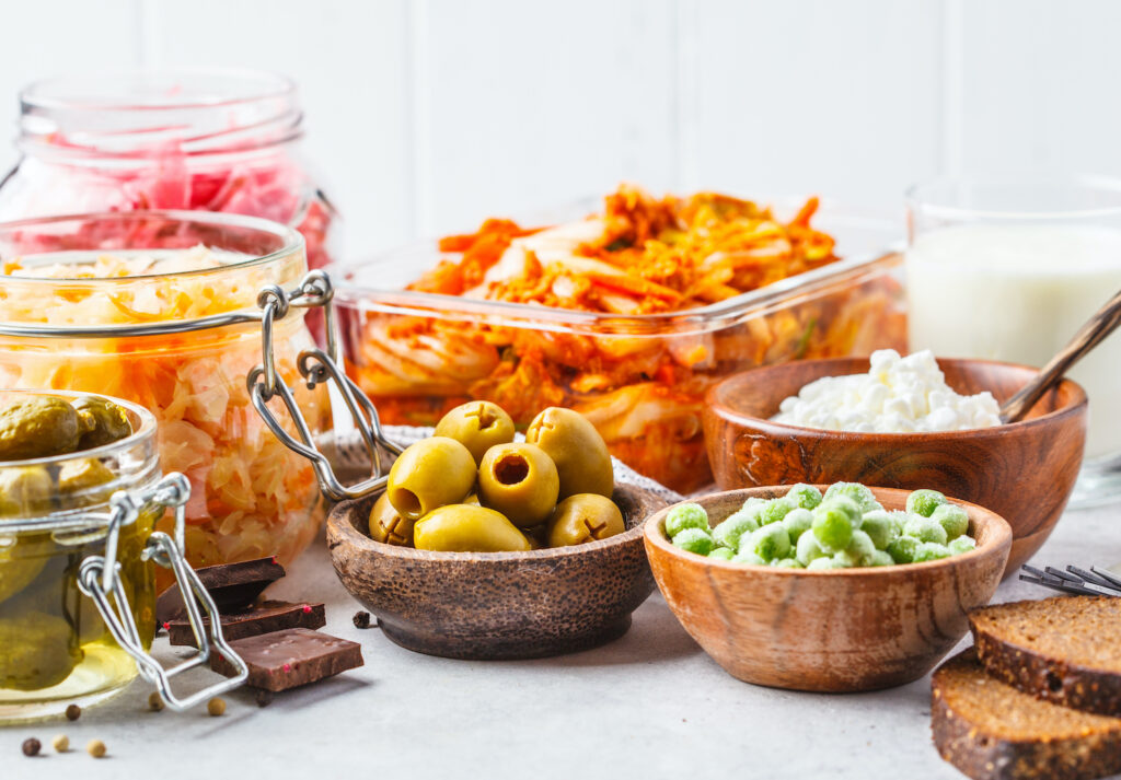 Probiotics food background. Kimchi, beet sauerkraut, sauerkraut, cottage cheese, olives, bread, chocolate, kefir and pickled cucumbers in glass jars, white background.