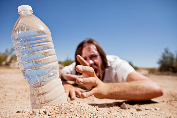 Dehydrated man crawling through the desert reaching for bottle of water.