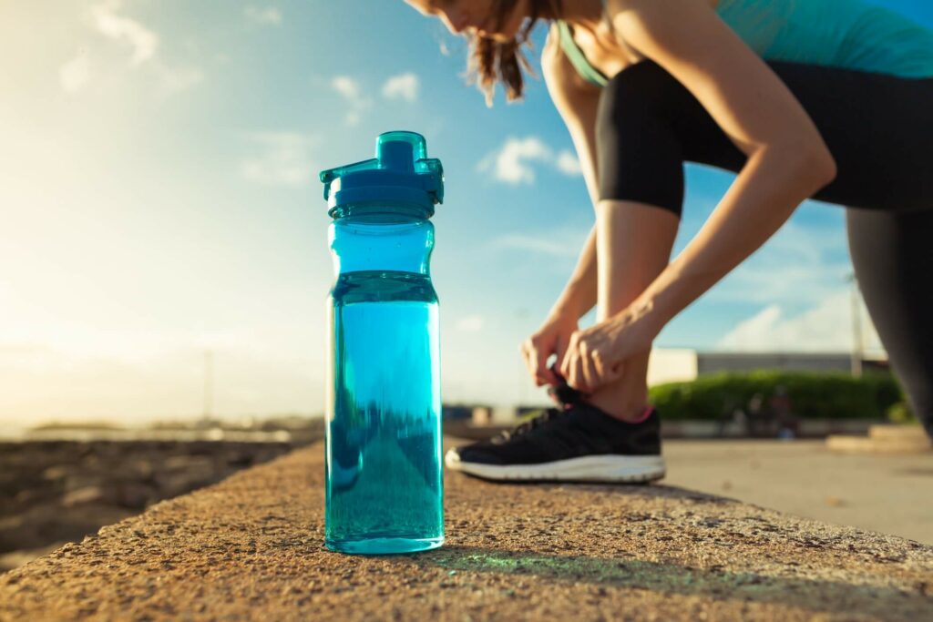 a woman adjusting her sport shoe with a bottle of water in her front