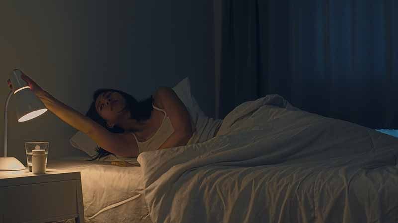 A woman switching on reading lamp before sleeping