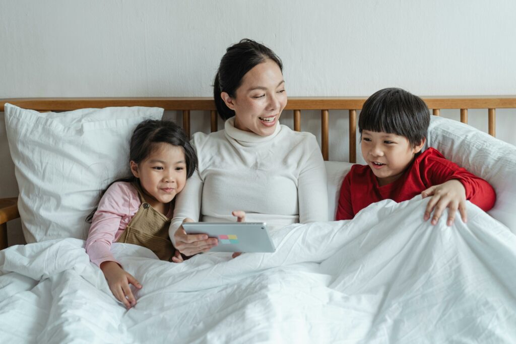 a mother teaching her two kids on the phone while sitting on the bed