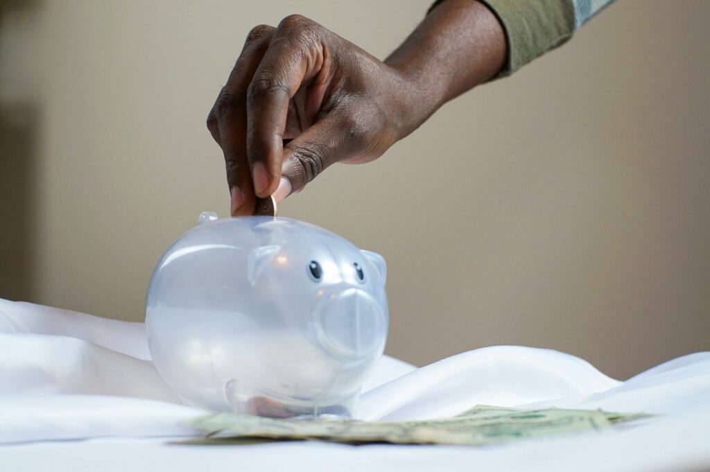 a hand dropping money into a piggy bank