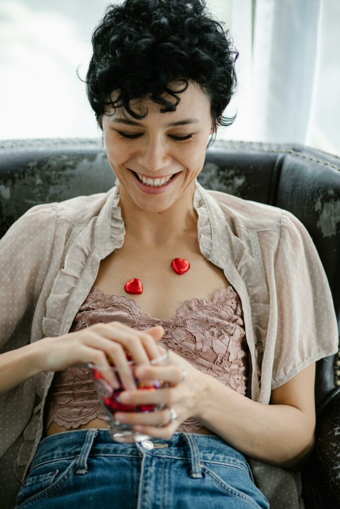 Joyful young ethnic female putting heart shaped candies on body and smiling