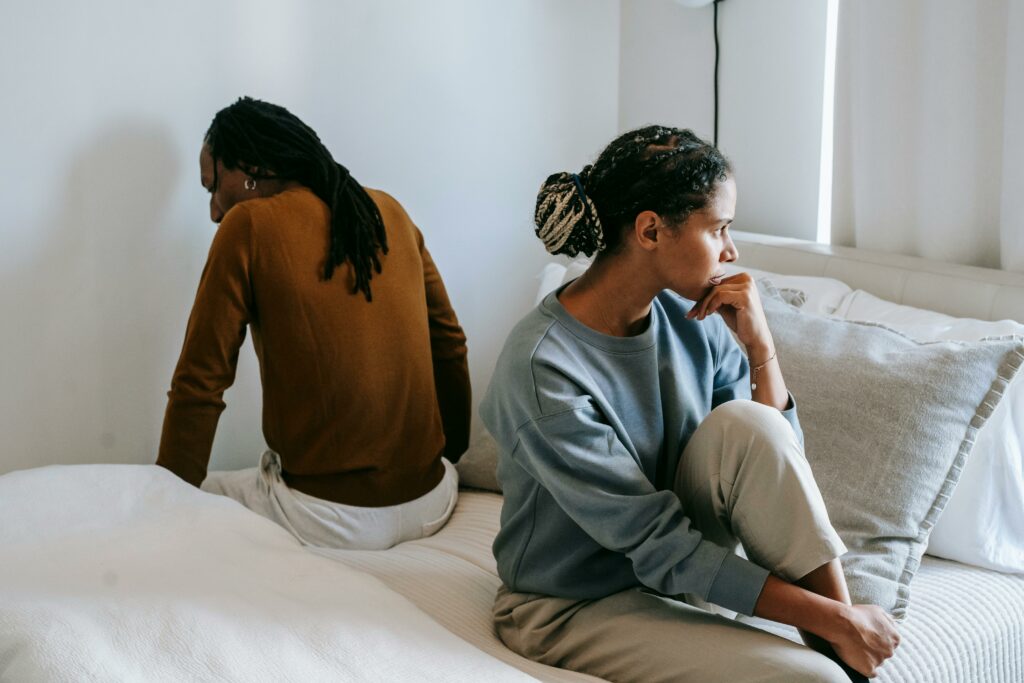 Displeased black woman with unrecognizable husband during conflict on bed