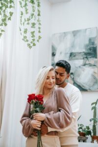 Man in White Sweater Hugging Woman in Brown Long Sleeve Shirt Holding Red Roses