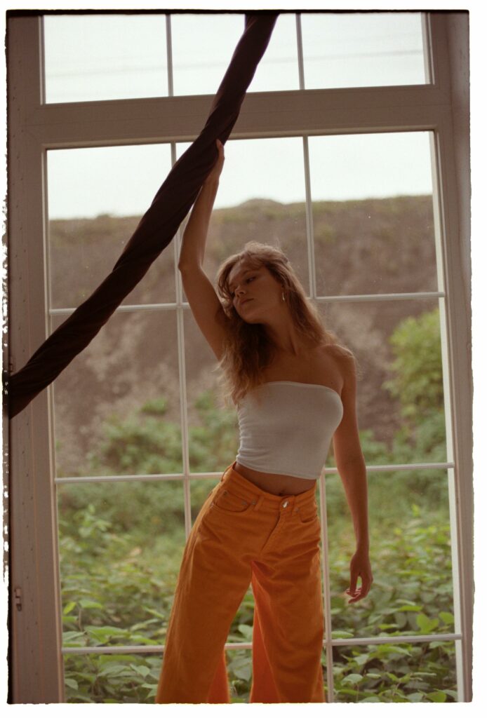 Woman in White Tube Top and Orange Pants Standing by the Window