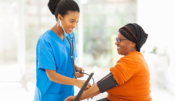 smiling african nurse checking senior patient's blood pressure